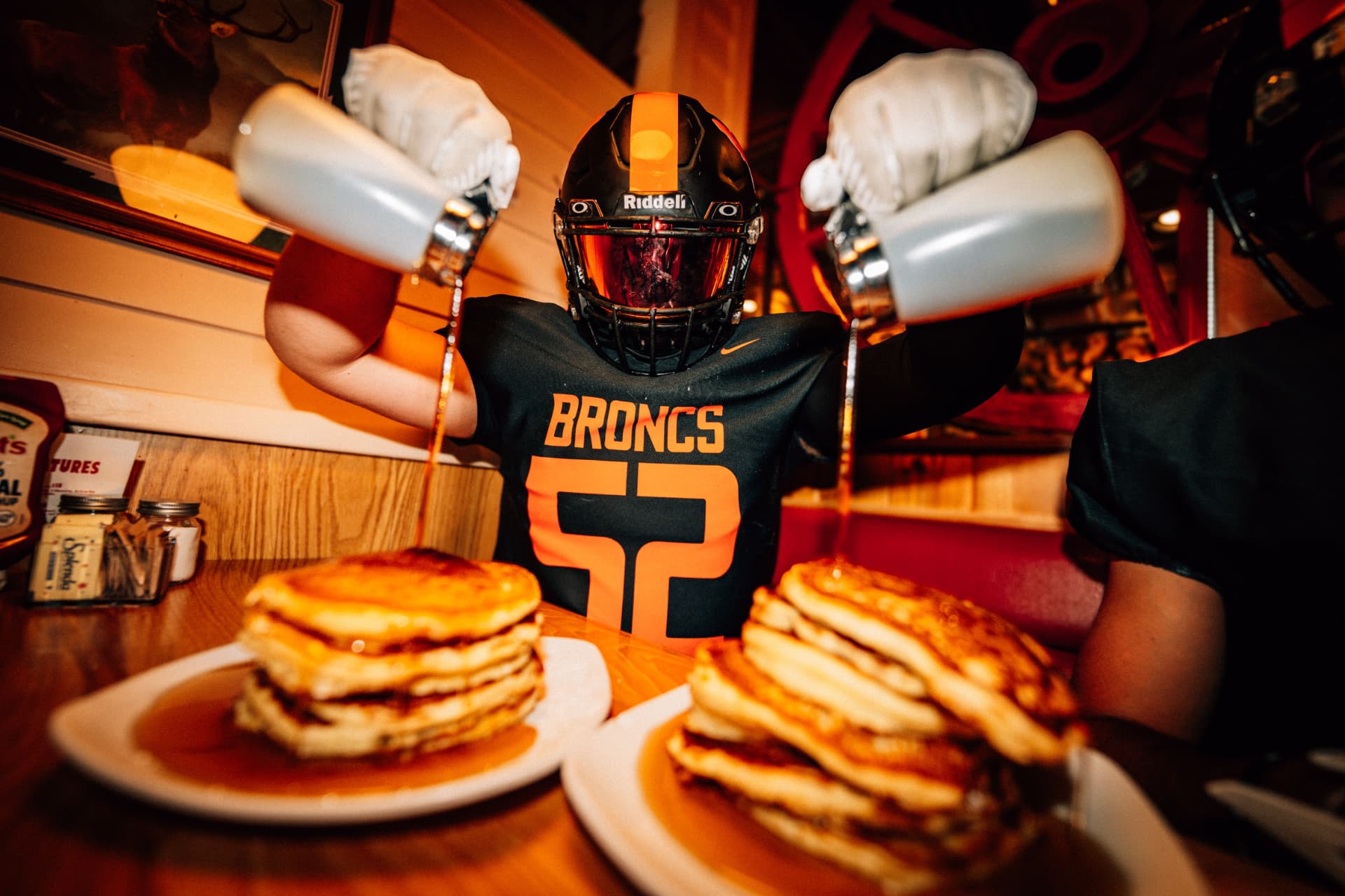Broncs player pouring syrup on pancake stacks at a sponsor diner