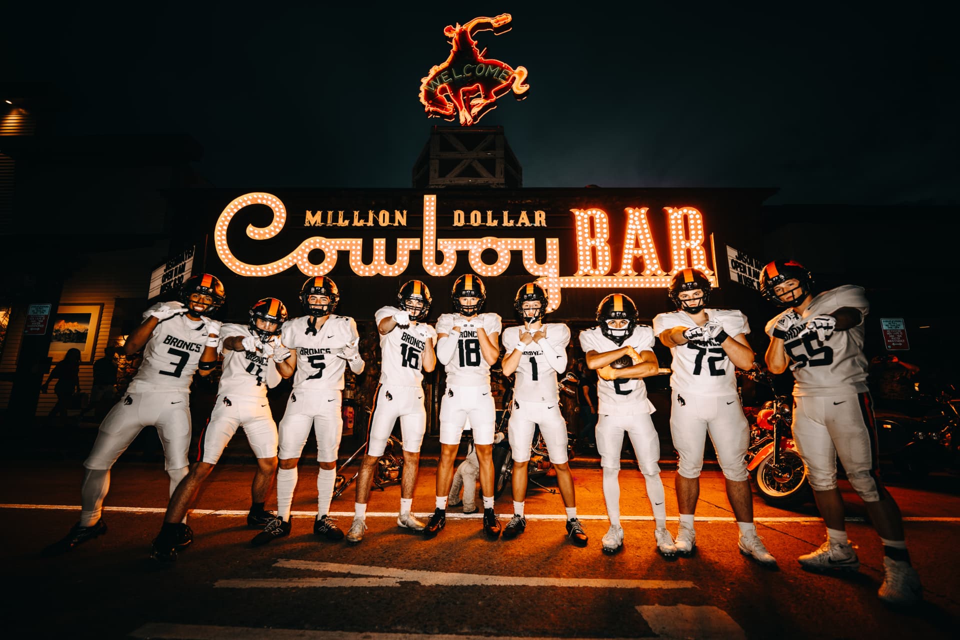 Broncs players posing under a lit-up Million Dollar Cowboy Bar sign